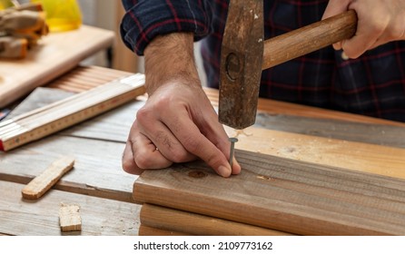 Carpenter Nail Wood. Male Hand Hold Hammer And Nail, Work Bench Table Background. DIY, Home Repair And Fix.