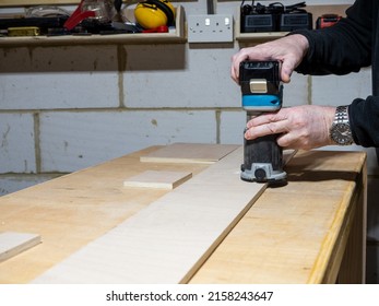 Carpenter operating a cordless battery powered trimming router  to add a bevel to the edge of a board