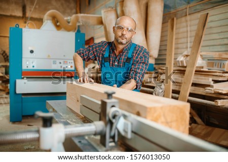 Carpenter processes wooden beam on plane machine