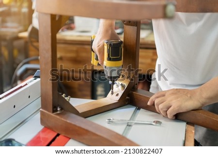 carpenter repair chair and using electric screwdriver at workshop, furniture restoration woodworking concept. selective focus