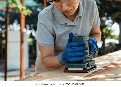 Carpenter Is Sanding A Plank Of Wood Using An Electric Sander Outdoors On A Sunny Day. Woman Does Hard Physical Work. Concept Of Gender Equality At Work. Craftsmanship And Woodworking - Powered by Shutterstock