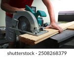 Carpenter sawing wood with handsaw. Carpenter working with a circular saw outside in sunny day. Wood chips flying.