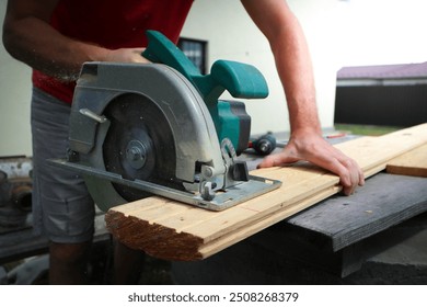 Carpenter sawing wood with handsaw. Carpenter working with a circular saw outside in sunny day. Wood chips flying. - Powered by Shutterstock