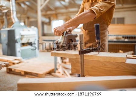 Carpenter sawing wooden bars with cordless electric saw at the joiner's workshop