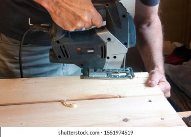 A carpenter saws a board with an electric jigsaw machine in a carpentry workshop. Close up hand with a jigsaw. Joinery production and concept. - Shutterstock ID 1551974519