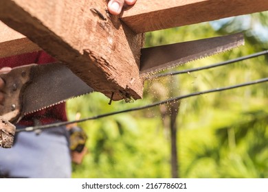 A carpenter saws off the excess edge of a wood rafter. Building or reconstructing a wooden roof frame for a rural home.