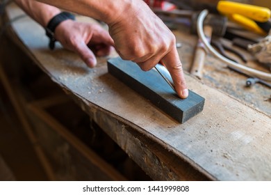 Carpenter sharpening a chisel in a small workshop, focus on the index finger.