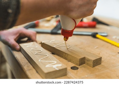 Carpintero presionando pegamento en dos trozos de madera con una mano. Cierre del proceso de madera. Mesa del taller con herramientas en segundo plano. Foto de alta calidad