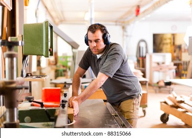 Carpenter is standing on electric cutter with ear protection