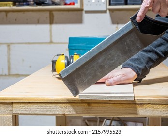 Carpenter trimming a construction  joint on a plywood board using a tenon saw