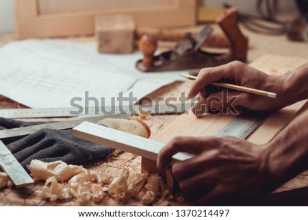 Carpenter uses a framing square for marking a line in a wooden plank.