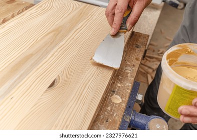 Carpenter uses putty to smooth out the knots in a wooden board. Recovery background. - Shutterstock ID 2327976621