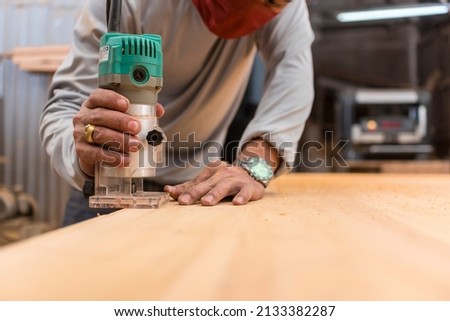 A carpenter uses a wood trimmer to chamfer to edge of a desk. Compact Wood Palm Router Tool. At a furniture making workshop.
