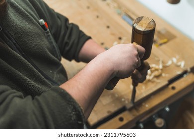 Carpenter using a chisel and a hammer to carve wood on a carpentry workbench. High quality photo