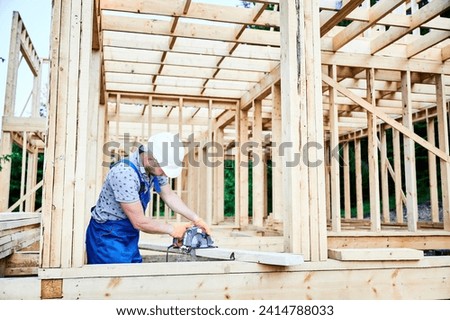 Carpenter using circular saw for cutting wooden plank. Man worker building wooden frame house. The idea behind modern ecological construction.