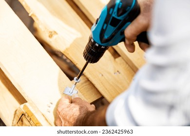 Carpenter using a cordless screwdriver to drill a wooden plank, Hands of caucasian worker drilling a wooden plank with a cordless electric drill, close-up outdoors