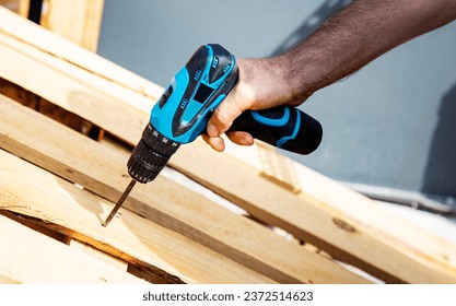 Carpenter using a cordless screwdriver to drill a wooden plank, Hands of caucasian worker drilling a wooden plank with a cordless electric drill, close-up outdoors - Powered by Shutterstock