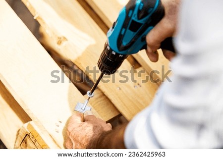 Carpenter using a cordless screwdriver to drill a wooden plank, Hands of caucasian worker drilling a wooden plank with a cordless electric drill, close-up outdoors