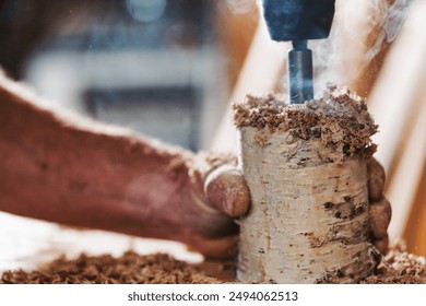 Carpenter is using a drill press to drill a hole in a piece of birchwood, with sawdust flying through the air. The image highlights the craftsmanship and precision involved in woodworking - Powered by Shutterstock