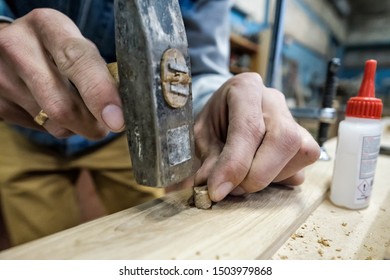 Carpenter using hammer, glue and wooden dowel. Close up view