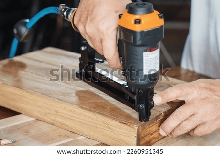 carpenter using nail gun or brad nailer tool on wood box in a workshop ,furniture restoration woodworking concept. selective focus