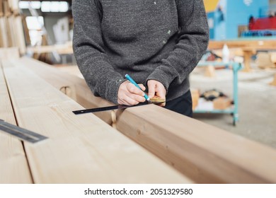 Carpenter Using A Right Angle Tool Or Carpenters Square On A Long Beam Of Wood In A Woodworking Factory In A Close Up On His Hands