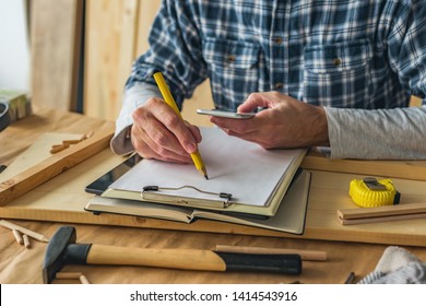 Carpenter Using Smart Phone To Complete Project To Do List In Small Business Woodwork Workshop