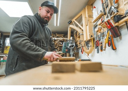 Carpenter using a wooden brush to clean two wooden planks placed on a workbench. High quality photo