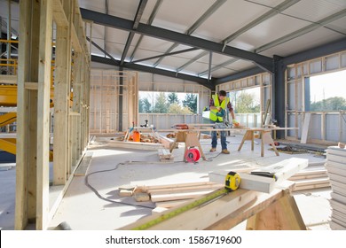 Carpenter Wearing Hi Viz Cutting Wood With Circular Power Saw In Building Construction Site Interior