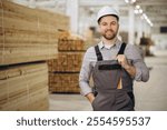 Carpenter wearing overalls and hardhat smiling and supervising wood production in a lumber warehouse, modular building industry