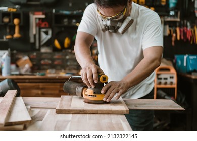 carpenter wearing protective equipment mask and Glasses using a random orbit sander on wood in the workshop,woodworking concept , selective focus - Shutterstock ID 2132322145