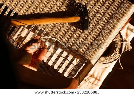 A carpenter weaving a new seat for a vintage danish chair with paper cord handcraft in a workshop natural sunlight warm atmosphere