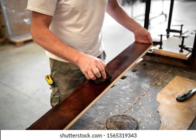 Carpenter or woodworker staining or coloring a briar root panel in a close up on the plank of wood and his hands over the workbench