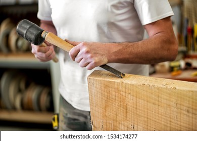 Carpenter or woodworker working with a chisel cutting or carving a block of wood with the beveled blade in a woodworking workshop in a close up on his hands