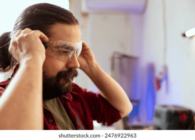 Carpenter in woodworking shop putting on protection glasses before assembling furniture. Cabinetmaker preparing safety equipment in joinery before starting work, close up shot - Powered by Shutterstock