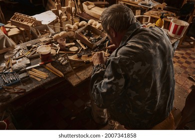 Carpenter at work. Rear view of an old craftsman making a wooden model of sail ship in his home workshop.