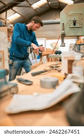 Carpenter At Workbench In Workshop Using Cordless Electric Drill
