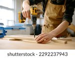 Carpenter working with drill leaning over table at carpentry workshop