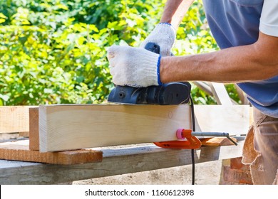 Carpenter working with electric planer on wooden plank in outdoor.