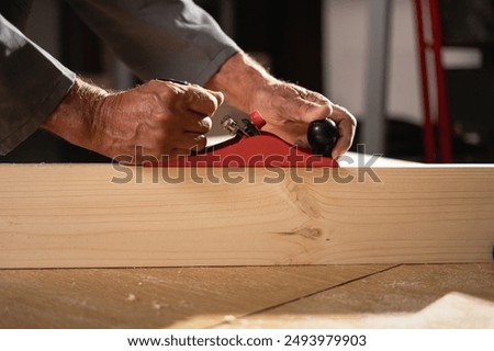 Carpenter working with jointer and plank in his workshop, close-up.