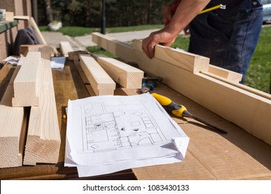 Carpenter Working With Technical Blueprint Drawing Construction Paper Lying On Outdoor Workshop Desk,surrounded With Carpentry Tools & Wood,furniture Making Pastime,cabin Or House Renovation Process