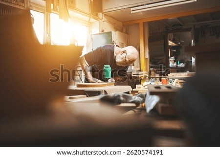 Carpenter working with tools and equipment on woodwork table in a workshop. Senior man with DIY carpentry skills using wood and power tool making, fixing objects or furniture in handicraft industry