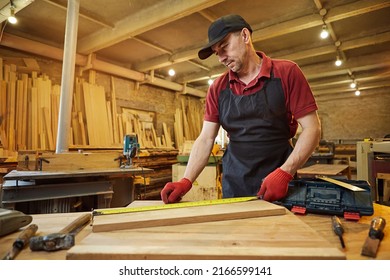 Carpenter working with a wood, marking plank with a pencil and taking measurements to cut a piece of wood to make a piece of furniture in a carpentry workshop - Powered by Shutterstock