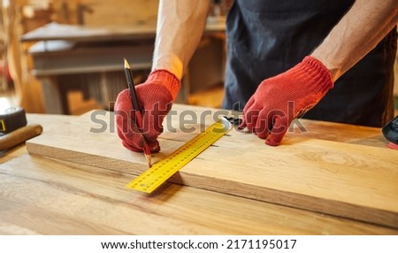 Carpenter working with a wood, marking plank with a pencil and taking measurements to cut a piece of wood to make a piece of furniture in a carpentry workshop, close-up view