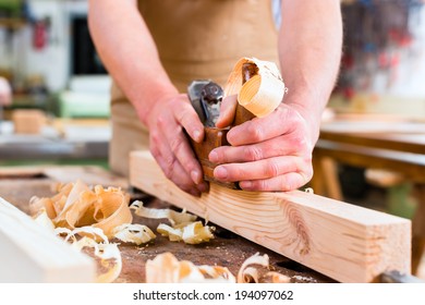 Carpenter working with a wood planer on workpiece in his workshop or carpentry