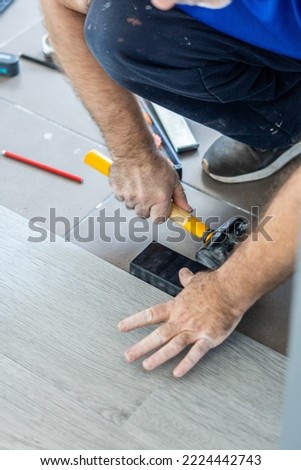 Carpenter works laying sheets of vinyl parquet hitting with a rubber mallet