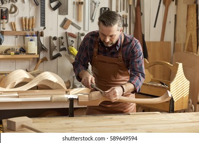 Carpenter Works With A Planer In A Workshop For The Production Of Vintage Furniture. He Makes Cabriole Leg For A Table In The Style Of Louis XV, Queen Anne/Joiner Makes Cabriole Leg For Vintage Table