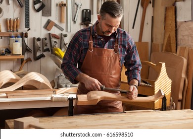 Carpenter Works With A Planer In A Workshop For The Production Of Vintage Furniture. He Makes Cabriole Leg For A Table In The Style Of Queen Anne/Joiner Makes Cabriole Leg For Vintage Table