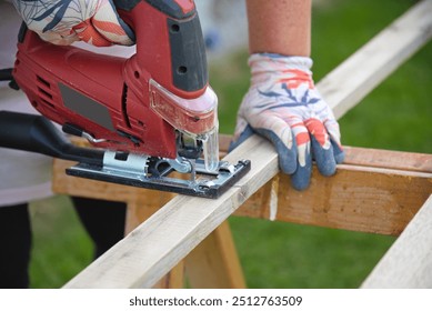 Carpenter works with wood with jigsaw - craftswoman with gloves saws through board - Powered by Shutterstock