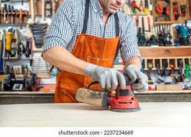 CARPENTER IN WORKSHOP WORKING WOOD WITH AN ORBITAL SANDER. SMALL BUSINESSES AND SELF EMPLOYED. DIY CONCEPT.
